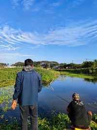 Rear view of man standing by lake against sky