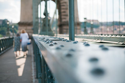 Metal railing on bridge with women walking in background