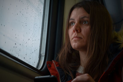 Young woman window transport. a thoughtful dark-haired girl looks out the window with raindrops