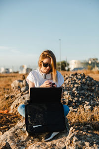 Young man using mobile phone while sitting on land