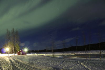 House on snow covered field against sky at night