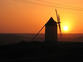 Traditional windmill on mountain against sky during sunset