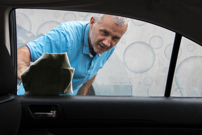 Satisfied mature man polishing his car with microfiber cloth. close-up