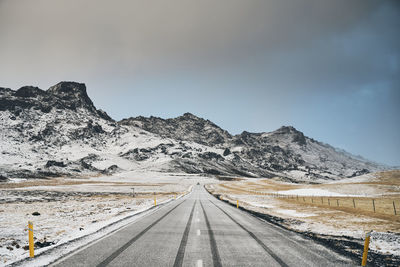 Road leading towards snowcapped mountains against sky