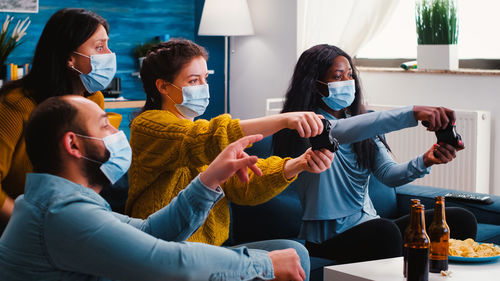 Cheerful people wearing mask while playing video game at home