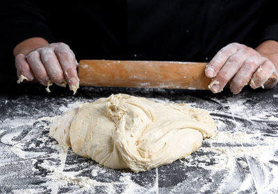 Midsection of person preparing dough against black background