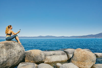 Young woman sitting by lake tahoe reading a kindle book during the day