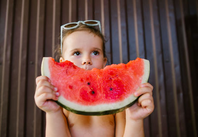 Low angle view of shirtless girl eating watermelon against wall