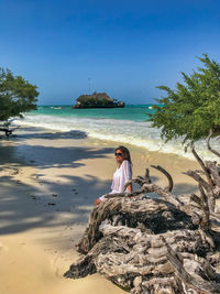 Woman standing by driftwood at beach against sky