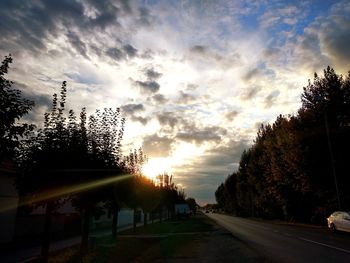 Street amidst trees against sky during sunset