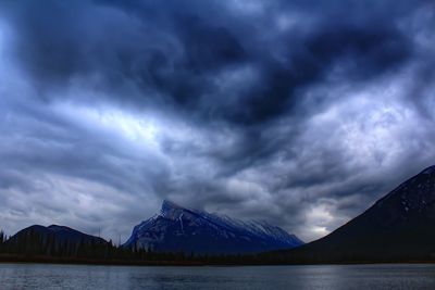 Scenic view of mt rundle by lake against cloudy sky