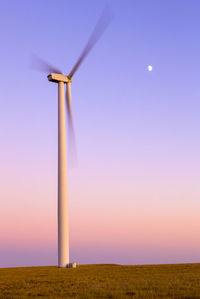 Wind turbine in motion against purple sky with moon