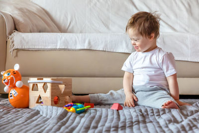 Disabled cute boy sitting with toys on carpet at home