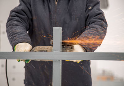 Midsection of man cutting metal in factory