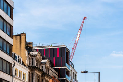 Low angle view of crane by building against sky