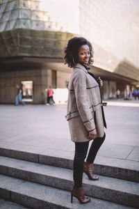 Beautiful african american young woman with afro and large hoop earrings in a stylish coat, smiling