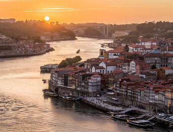 Boats moored in sea by city against sky during sunset