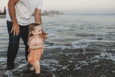 Toddler girl splashing in ocean with father at sunset