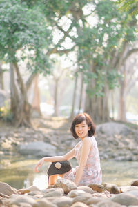 Young woman sitting on land against trees