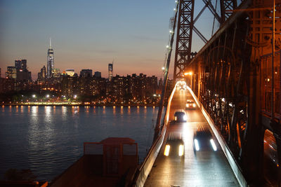 Illuminated manhattan against sky seen from williamsburg bridge over east river