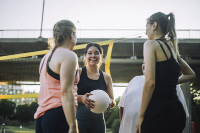 Low angle view of smiling woman holding volleyball with female friends