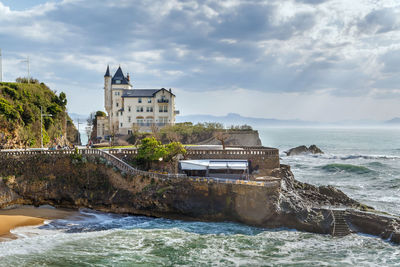 Buildings by sea against cloudy sky