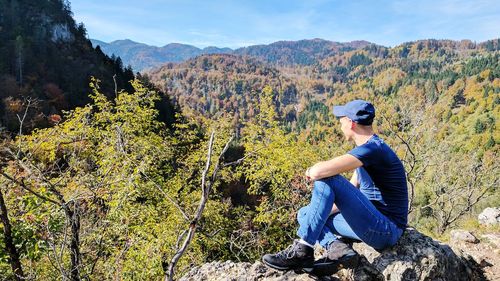 Rear view of man sitting on rock against sky