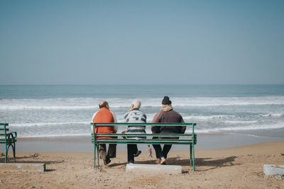 Rear view of people on beach against clear sky