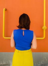 Rear view of woman standing against orange wall