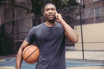 Young man talking on mobile phone while standing in basketball court