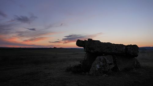 Stone wall on landscape against sky during sunset