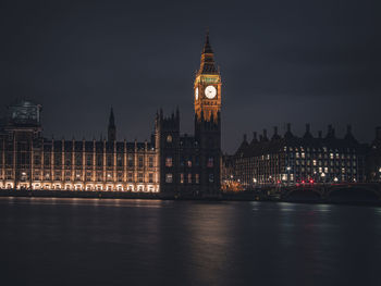 Big ben by river against sky in city at night