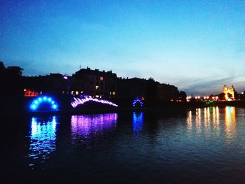 Illuminated buildings by river against sky at night