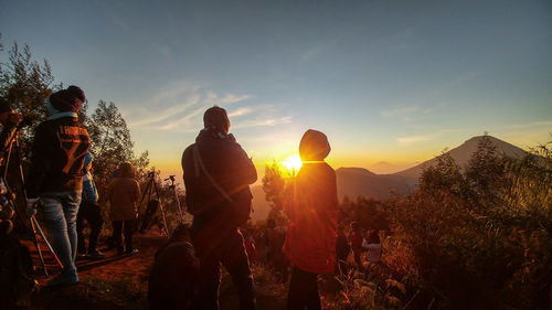 People standing on mountain against sky during sunset