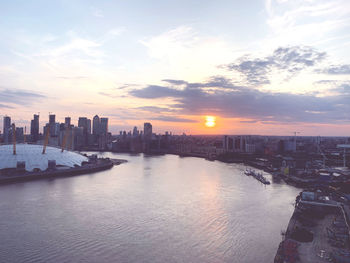 Scenic view of river by buildings against sky during sunset