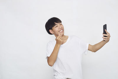 Smiling young man using smart phone against white background