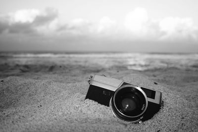 Close-up of camera on sand at beach against sky