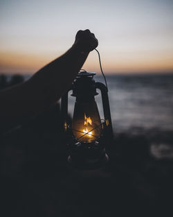 Close-up of illuminated lamp on beach against sky during sunset