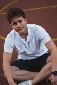 High angle portrait of young man sitting on basketball court