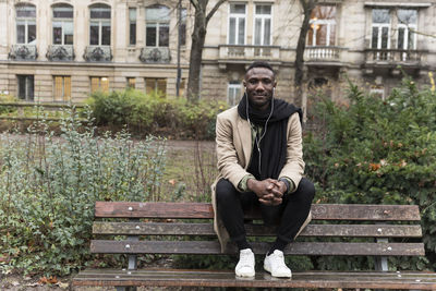 Portrait of young man listening music while sitting on bench