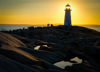 Peggys point lighthouse on rock formation against orange sky during sunset