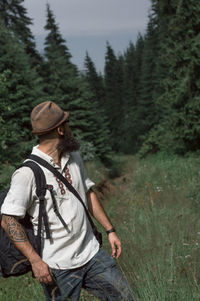 Male hiker with backpack standing on grassy field in forest