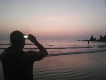 Silhouette woman standing on beach against sky during sunset