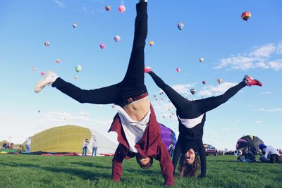 Friends doing handstand on grassy field against hot air balloons in sky