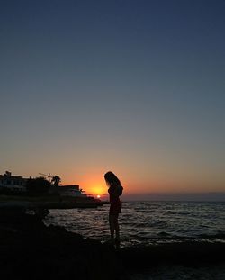 Silhouette woman standing on beach against clear sky during sunset