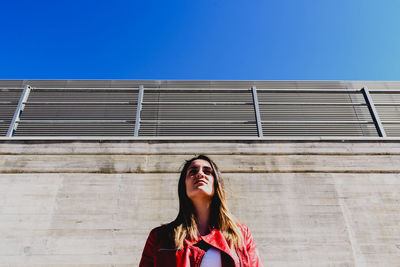 Low angle view of young woman standing against wall