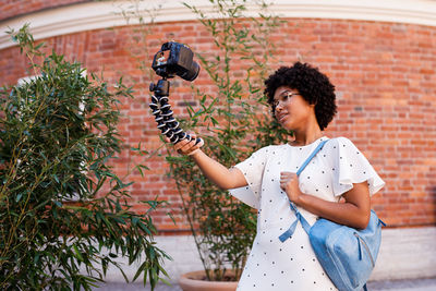 Teenage girl taking selfie through camera while standing against brick wall