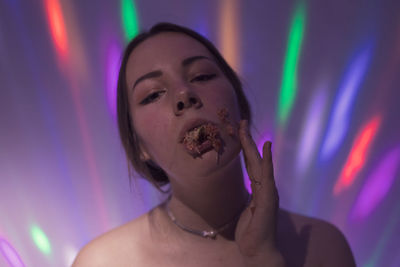 Close-up portrait of young woman eating fruit against wall