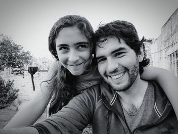 Portrait of smiling young woman using phone against sky