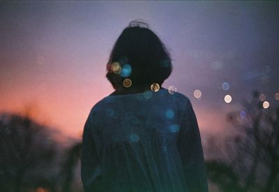 Rear view of woman standing against sky during sunset